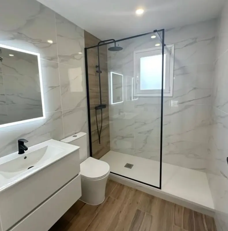 Ducha con mampara de vidrio fija en baño de mármol blanco