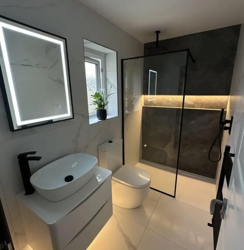 Baño en suite con mampara de vidrio y revestimiento en tonos oscuros